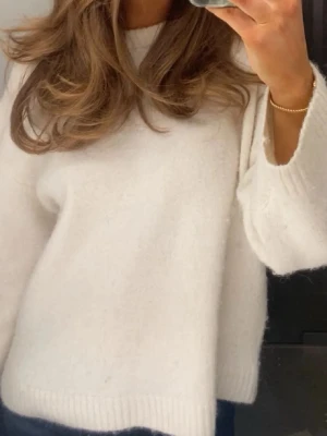 Vit stickad tröja - Mysig vit stickad tröja med rund hals och långa ärmar. Tröjan har en fluffig och mjuk känsla, samt ribbade muddar vid ärmslut och nederkant. Perfekt för lager på lager och enkel att matcha med jeans eller kjol. 