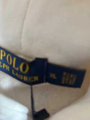 Vit teddyjacka från Polo Ralph Lauren - Mysig vit teddyjacka från Polo Ralph Lauren i storlek XL. Jackan har en fluffig och mjuk känsla som ger en avslappnad och trendig look. Perfekt för dig som vill ha en stilren och bekväm jacka till vardags.
