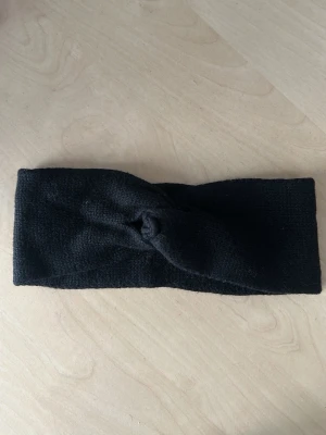 Svart stickat pannband twistdetalj - Snyggt svart stickat pannband med twistdetalj framtill. Perfekt för att hålla håret på plats och värma öronen under kyliga dagar. Mjuk och stretchig kvalitet som sitter bekvämt på huvudet. Passar till de flesta stilar och är lätt att matcha.