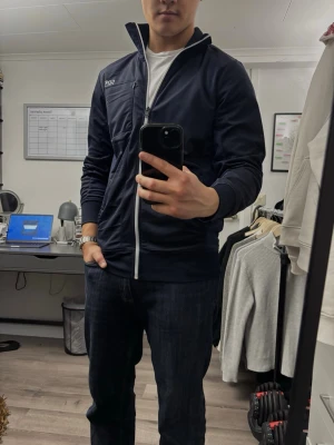 Marinblå ziptröja från Core Sports - Snygg marinblå ziptröja från Core Sports med vit dragkedja och hög krage. Tröjan har långa ärmar, diskret logga på bröstet och ribbade muddar. Perfekt till chill eller träning, tillverkad i mjukt material för extra komfort.