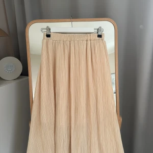 Plisserad beige långkjol från otherstories - Säljer en beige plisserad långkjol med elastisk midja. Kjolen har en flowy passform och tunna vertikala veck som ger ett snyggt fall. Perfekt att styla med en enkel topp eller stickad tröja. En liten fläck vid resoret men annars jättefin!