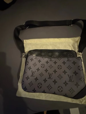 Louis Vuitton Monogram axelväska - Snygg axelväska från Louis Vuitton i svart och grått med klassiskt monogrammönster. Väskan har justerbar axelrem i textil och detaljer i läder. Perfekt storlek för det viktigaste och ger en lyxig känsla till din outfit.