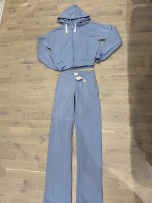 Ljusblått set från Gina Tricot, xs tall - Säljer ett ljusblått mjukisset från Gina Tricot i storlek XS. Setet består av en croppad hoodie med dragkedja och huva samt ett par matchande byxor med dragsko i midjan. Materialet är mjukt och skönt, perfekt för chill dagar hemma. Modell Tall så dom är länge i benen