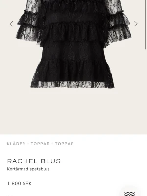 Svart spetsblus med volanger - Trendig svart blus i spets från By Malina med flera lager volanger och transparenta detaljer. Blusen har korta ärmar och hög hals, perfekt för dig som gillar en romantisk och edgy stil. Materialet är tunn spets som ger en luftig känsla.