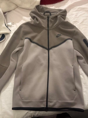 Nike Tech Fleece hoodie - Nike Tech Fleece hoodie aldrig använt den i två nyanser av grått med hel dragkedja och svart Nike-logga på bröstet. Hoodien har huva, två sidofickor och en modern, sportig design. Tillverkad i mjukt och bekvämt fleecematerial som passar perfekt för en avslappnad stil. Passar även xs då den bara sitter lite baggy då