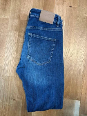 Blå slim jeans från Dobber - Snygga blå jeans från Dobber med klassisk femficksdesign och raka ben. Jeansen har en mörk tvätt och en bakficka utan detaljer. W31 l32 passar w30 l32. Perfekta till en avslappnad stil och tillverkade i slitstarkt denimtyg.