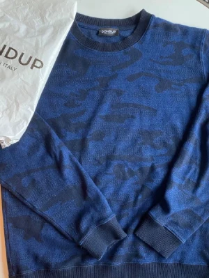 Sällsynt Blå tröja från Dondup - Snygg blå tröja från Dondup med mörkblått camo-mönster. Tröjan har rund halsringning, ribbade muddar vid ärmslut och nederkant samt en avslappnad passform. Perfekt för dig som gillar streetwear och vill ha något unikt i garderoben. NYPRIS:4599Kr