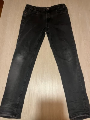Svarta slim fit jeans från Zara - Säljer ett par svarta slim fit jeans från Zara med klassisk femficksdesign och knappgylf. Jeansen har en lätt tvättad look och raka ben. Perfekta till en avslappnad streetstyle eller vardagsoutfit.
