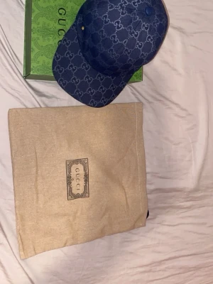 Blå GG Supreme keps från Gucci - Säljer en blå keps från Gucci med det klassiska GG Supreme-mönstret över hela kepsen. Kepsen har böjd skärm och justerbar rem bak. Materialet är canvas med exklusiv känsla och kepsen kommer med original dustbag och grön Gucci-box.