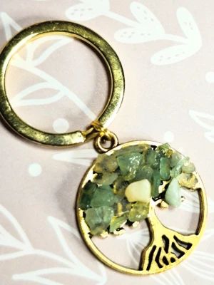 Nyckelring med livets träd och gröna kristaller aventurin - Unik nyckelring i guldfärgad metall med ett runt hänge format som ett träd. Trädkronan är dekorerad med små gröna och ljusa stenar som ger en naturlig och bohemisk känsla. Perfekt accessoar för dig som gillar detaljer och naturinspirerad design.