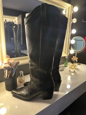 Svarta höga cowboy boots - Snygga svarta cowboy boots med klassiska broderade detaljer och spetsig tå. 