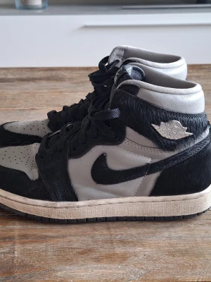 Nike Air Jordan 1 Retro High OG Twist 2.0 stl 38 - Säljer ett par Air Jordan 1 High sneakers från Nike i svart och grått. Skorna har en unik textur med hårigt material på vissa partier, klassisk swoosh och vingslogga på sidan. Perfekt för dig som vill sticka ut med en ikonisk och cool modell.