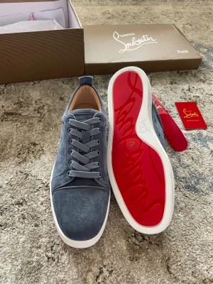 Louboutin skor - Snygga blå sneakers i mocka från Christian Louboutin med klassisk röd sula och vita kanter. Skorna har rund tå, matchande blå skosnören och diskreta sömdetaljer. Perfekta för dig som vill ha en exklusiv touch på din outfit.