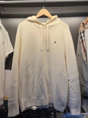 hoodie från Morris - Snygg krämvit hoodie från Morris med liten broderad logga på bröstet. Tillverkad i mjukt stickat material och har ribbade muddar samt dragsko i huvan. Perfekt för en clean och stilren look. Tröjan är helt ny och endast använd 1 gång 