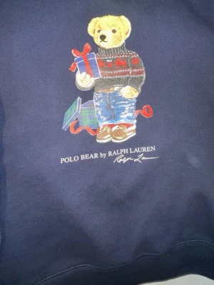 ( äkta) Mörkblå Polo Bear stickad tröja - Mörkblå stickad tröja från Ralph Lauren med ikoniska Polo Bear-trycket framtill. Tröjan har rund halsringning och långa ärmar. Perfekt för dig som gillar klassisk och lekfull stil. ( storlek s men passar även till m) 