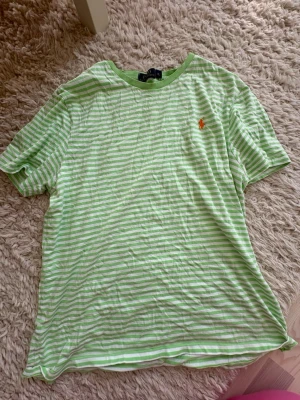 Polo t shirt - Fräsch t-shirt från Polo Ralph Lauren med ljusgröna och vita ränder. Klassisk kortärmad modell med rund hals och orange broderad logga på bröstet. Perfekt för dig som gillar stilrena och sportiga plagg. Materialet är mjuk bomull.