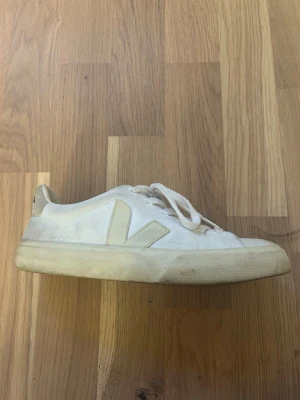 Vita Veja sneakers med logga - Stilrena vita sneakers från Veja med den klassiska V-loggan på sidan. Skorna har låga kanter, vita snören och en tjock vit sula. Tillverkade i canvas och gummi för en clean och modern look.