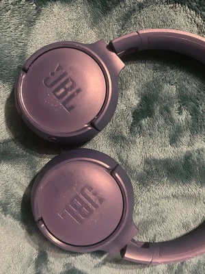 Lila over-ear hörlurar från JBL - Säljer ett par lila over-ear hörlurar från JBL med mjuka öronkuddar och tydlig logga på kåporna. Hörlurarna har en rund och stilren design med justerbar båge och är tillverkade i plast och konstläder. Pads are little worn out and some scratches but work good