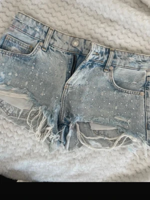 Ljusa denimshorts med slitningar - Jättefina ljusblåa jeans shorts med typ som pärlor på sig. Har en liten defekt på ena skärpöglan men väldigt lätt att fixa❤️hör av dig vid frågor❤️Midjemått : 38 cm rakt över