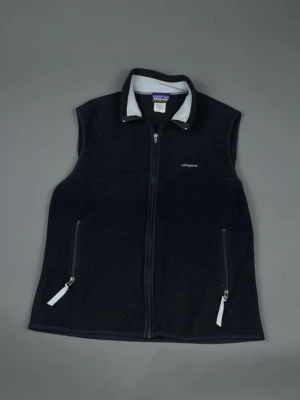 Svart fleeceväst från Patagonia Storlek L - Jag säljer en retroinspirerad fleeceväst från Patagonia. Det är ett riktigt vintageplagg som ser bra ut och passar perfekt in i outdoor/gorpcore-stilen. Plagget har normala tecken på slitage och mindre åldersdefekter.  Mått finns på bilderna. Etikettstorlek: L (Jag kan skicka ytterligare mått eller foton via privat meddelande för att vara säker.)  Perfekt för dig som letar efter kläder med själ. Jag är villig att ge rabatt på priser på set – kolla in min garderob så gör vi en bra affär!