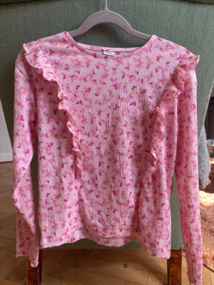 Rosa blus med volang från Lindex  - Rosa långärmad blus med fjärilsmönster och volanger från Lindex. Storlek 146/152.