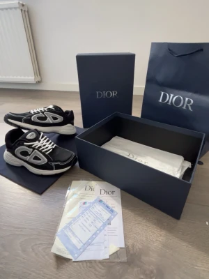 Dior svartvita sneakers med CD-logo - Säljer ett par snygga Dior sneakers i svart och vitt med tydlig CD-logo på sidan. Skorna har vita snören, tjock vit sula och är tillverkade i mesh och läder. Perfekt för dig som vill ha en exklusiv och trendig look. Levereras med originalkartong och påse.