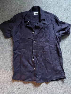 Mörk lila linneskjorta Massimo Dutti - Snygg mörk lila skjorta från Massimo Dutti i 100% linne. Skjortan har korta ärmar, klassisk krage, bröstficka och knappar framtill. Perfekt för en avslappnad och stilren look.