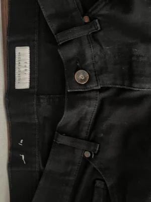 Svarta jeans från Tiger of Sweden - Snygga svarta jeans från Tiger of Sweden med klassisk femficksmodell och raka ben. Jeansen har metallknapp och bälteshällor, perfekta för en stilren look. Materialet är bomull med stretch för extra komfort.