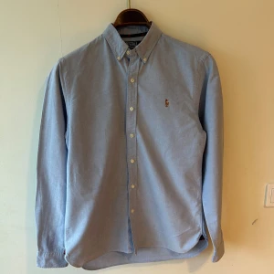 Blå skjorta från Polo Ralph Lauren M - Klassisk ljusblå skjorta från Polo Ralph Lauren i slim fit-modell. Skjortan har button-down krage, långa ärmar och broderad logga på bröstet. Tröjan är i storleken Medium.