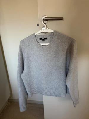 Ljusgrå stickad tröja från Uniqlo - Mysig ljusgrå stickad tröja från Uniqlo med rund halsringning och ribbade muddar vid ärmslut och nederkant. Enkel och stilren design som passar perfekt till lager på lager. Tillverkad i mjukt material för extra komfort.
