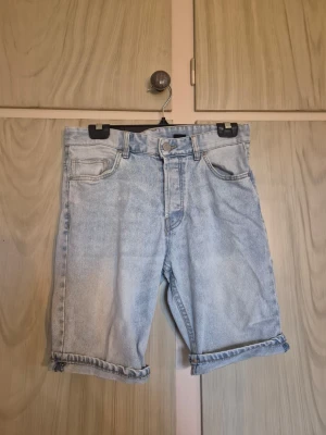 Ljusblå denimshorts med uppvik - Ljusblå denimshorts med klassisk femficksdesign och uppvikta benslut. Shortsens passform är normal och de har en knapp- och dragkedjeförslutning framtill. Perfekta för varma dagar och har en tidlös look som funkar till många stilar.     Alla kläder rollas innan dom skickas hem då det finns katt i hemmet🐈 Jag stryker och tvättar INTE innan jag skickar det får du stå för själv så det blir som du vill ha det🤗
