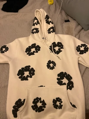 Denim tears xl men passar L - Säljer en vit hoodie från Denim Tears med stora svarta blomliknande mönster över hela tröjan. Hoodien har en stor huva med dragsko och en klassisk magficka. Materialet är mjukt och bekvämt, perfekt för dig som vill ha en unik och trendig look.