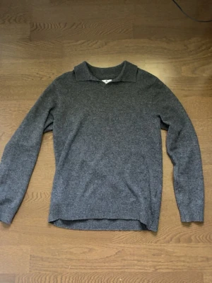 Grå stickad tröja med krage - Säljer en stilren grå stickad tröja med krage. Tröjan har långa ärmar och ribbstickade muddar vid ärmslut och nederkant. Perfekt för dig som vill ha en enkel och snygg look. Materialet känns mjukt och bekvämt.