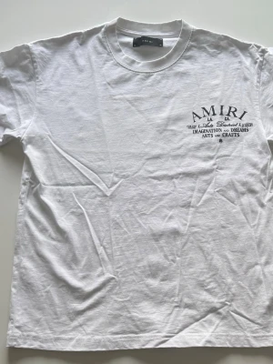 AMIRI Vit T-shirt - Vit t-shirt från AMIRI med svart tryck på både bröstet och ryggen. Klassisk rund hals och korta ärmar. Stort grafiskt print på ryggen. Tillverkad i bomull.
