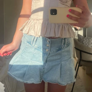 Ljusblå jeanskjol med knappar🩵 - Trendig ljusblå jeanskjol med hög midja och dekorativa knappar framtill. Kjolen har en kort och utsvängd modell med markerade sömmar och lätt tvättad look. Perfekt för dig som vill ha en cool och avslappnad stil.