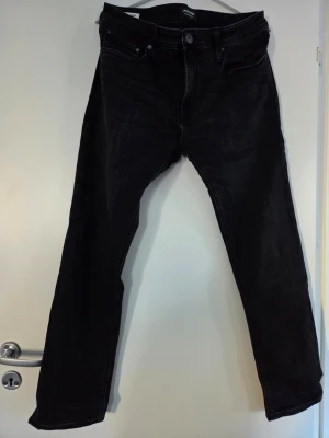 Svarta jeans med rak passform - Säljer ett par svarta jeans med klassisk rak passform och fem fickor. Jeansen har knapp- och dragkedjegylf samt tydliga sömmar. Perfekta för dig som gillar en enkel och stilren look.