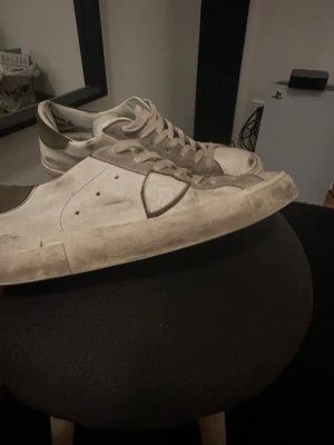 Vita sneakers från Philippe Model - Snygga vita sneakers från Philippe Model med grå detaljer och klassisk låg siluett. Skorna har ovandel i läder och mocka, samt en gummisula med tydligt mönster. Perfekta för en stilren och avslappnad look. Pris är ej hugget i sten 