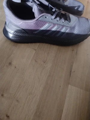 Gråa Adidas sneakers med svarta detaljer - Snygga Svarta sneakers från Adidas med klassiska tre ränder i silver på sidan och svart sula. Ovandelen är i textilmaterial och skon har en sportig, modern look. Perfekta för dig som gillar stilrena och bekväma sneakers.