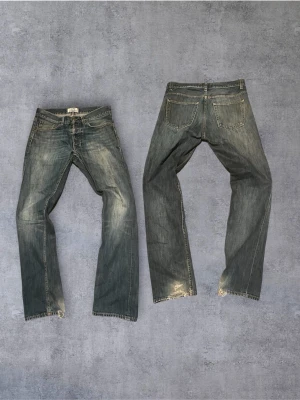 Vintage Acne Studios jeans - Säljer ett par klassiska blå jeans från Acne Studios med raka ben och slitningar vid benslut. Jeansen har fem fickor, knappgylf och snyggt tvättad finish som ger en avslappnad look. Perfekta för dig som gillar en tidlös och cool stil.