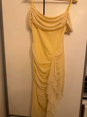 Ljusgul långklänning med volang - Säljer en elegant ljusgul långklänning med tunna axelband och draperad överdel. Klänningen har vackra volangdetaljer framtill och är tillverkad i ett lätt, flödande material som ger en romantisk känsla. Perfekt för dig som vill sticka ut med en feminin look.
