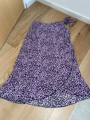 Lila leopardmönstrad omlottkjol - Säljer en snygg lila omlottkjol med leopardmönster och knyt i midjan. Kjolen har en längre modell och är perfekt för dig som vill sticka ut med ett trendigt mönster. Materialet känns lätt och flowy, vilket gör den superbekväm att bära.