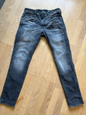 Svarta slim fit jeans från Replay - Snygga svarta slim fit jeans från Replay med slitningar och ljusare partier på benen. Klassisk femficksmodell med dragkedja och knapp i midjan. Jeansen har en modern passform och är tillverkade i bomullsdenim med lite stretch.
