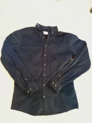 Svart skjorta från Lindbergh - Svart skjorta från Lindbergh med relaxed fit och klassisk krage. Skjortan har långa ärmar och knappar längs hela framsidan samt vid ärmsluten. Materialet är bomull och skjortan har en enkel, stilren design som passar till många olika outfits.