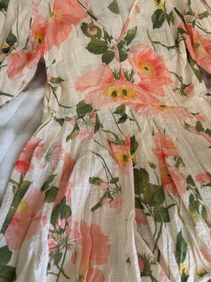 Blommig kortklänning  - Supersöt kortklänning i ljusbeige med stora blommor i rosa och grönt. Klänningen har v-ringning, puffiga trekvartsärmar med resår och ett flowy fall. Perfekt för sommarens alla tillfällen! Helt ny aldrig använt 🤍