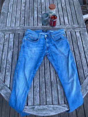 Blå jeans från Replay herrmodell - Säljer ett par klassiska blå jeans från Replay med snygg tvätt och raka ben. Jeansen har fem fickor, vita sömmar och Replay-logga på bakfickan. Materialet är denim i bomull och passformen är normal. Perfekta för en avslappnad och trendig stil.