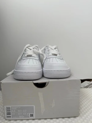 Nike Air Force 1 vita  - Klassiska Nike Air Force 1 sneakers i helvitt läder , vita skosnören och diskret Nike-logga på sidan. Tjock sula och metallbricka med AF1 på snörningen. Perfekta för en clean och stilren look.Dessutom så är boxen lite skadad men skorna är på top.