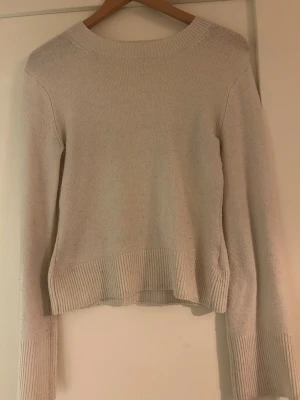 Beige stickad tröja med ribbade detaljer - En stilren beige stickad tröja med rund halsringning och ribbade muddar vid ärmslut och nederkant. Tröjan har en rak passform och är perfekt för lager på lager. Materialet känns mjukt och bekvämt mot huden.