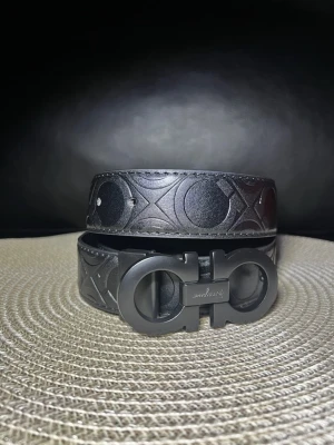 Ferragamo - Snyggt svart bälte med präglat mönster och spänne i matt svart. Bältet är gjort i skinn och har en modern, stilren look som passar till många outfits.