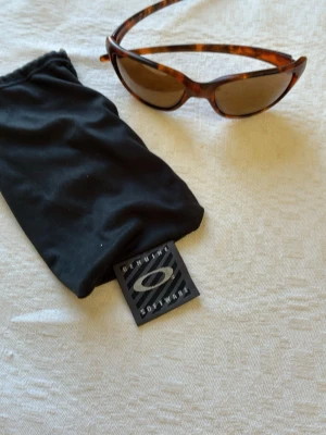  Oakley solglasögon  - Snygga solglasögon från Oakley med brunmelerat skal i cat eye-modell. Oakley logga på sidan av bågarna. Glasen är bruna och bågarna har ett klassiskt mönster som ger en cool vintagekänsla. Kommer med original svart mjukt fodral med Oakley-logga. Skador på insidan av glas. Syns inget framifrån. Går fint att köpa nya glas 
