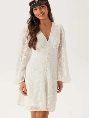 Studentklänning - Superfin vit kortklänning med v-ringning och långa, transparenta spetsärmar. Klänningen har knappar framtill och ett vackert blommigt spetsmönster över hela tyget 🌸. Perfekt för student eller sommarens festligheter. Klänningen är helt oanvänd med lappen kvar! Pris går att diskutera och kan även skicka mer bilder eller mått✨